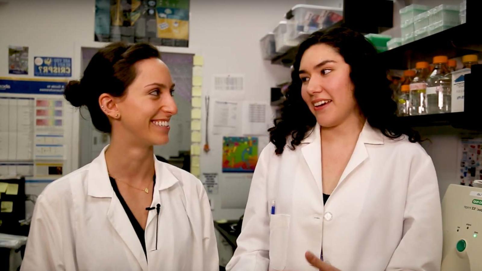 两个穿着实验室大褂的年轻女性在科学实验室里谈话