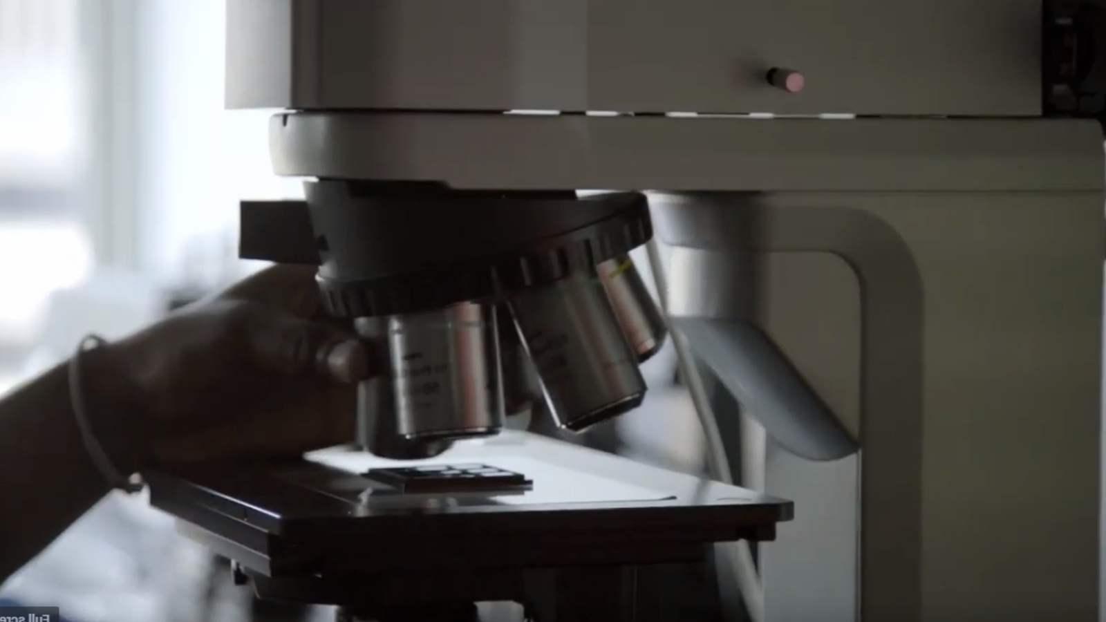 close up of a microscope and a hand positioning a slide