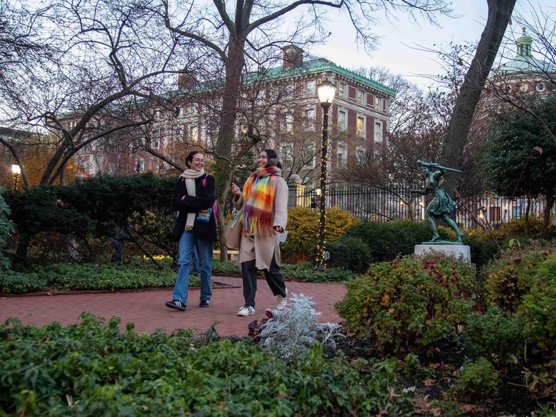 Students walk on Barnard campus with holiday lights and runner statue in background
