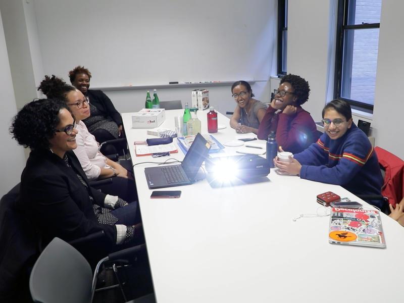 六名有色人种女性围坐在会议桌旁